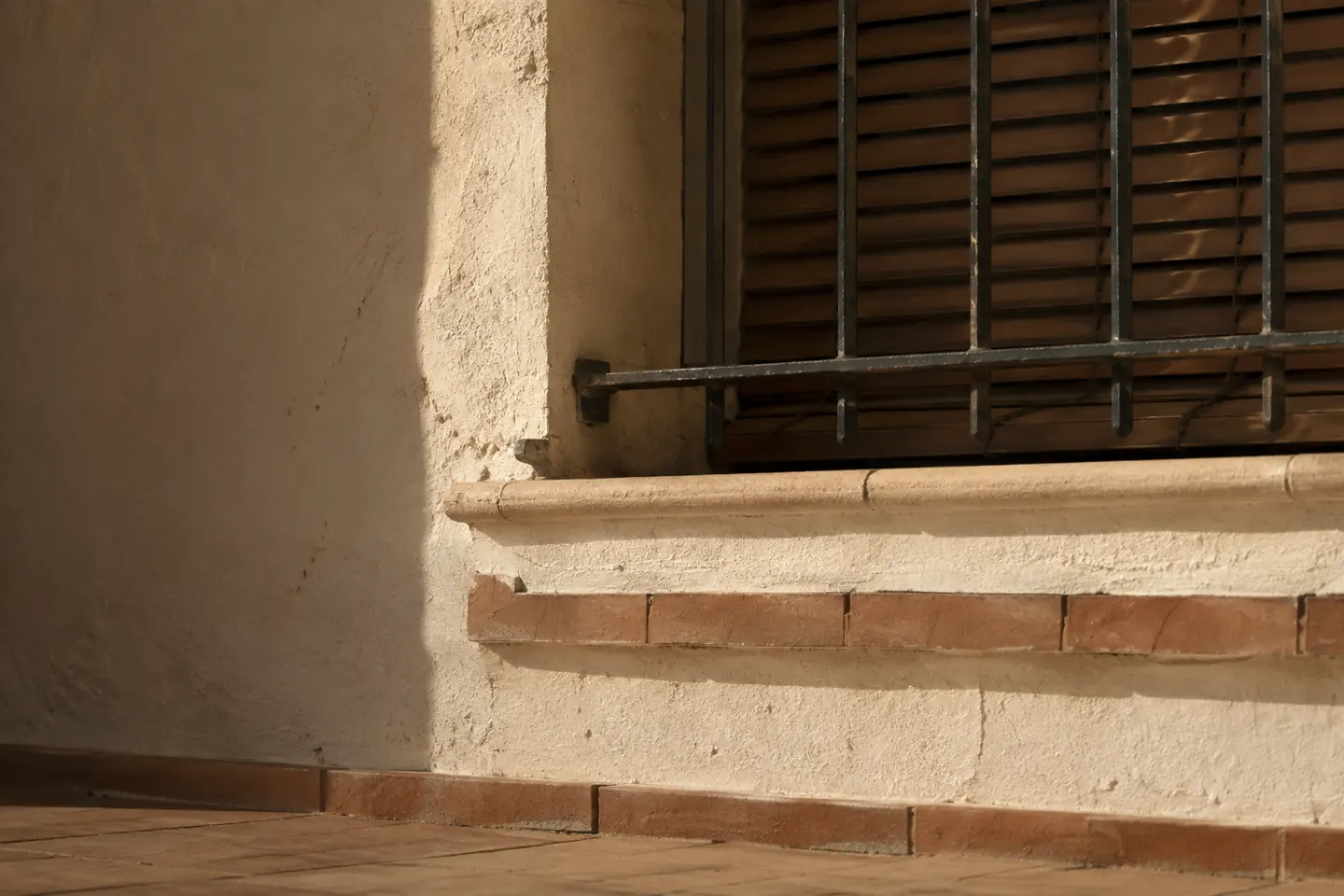 Detalle de una fachada residencial soleada con lamas exteriores, sombra profunda y ventana protegida