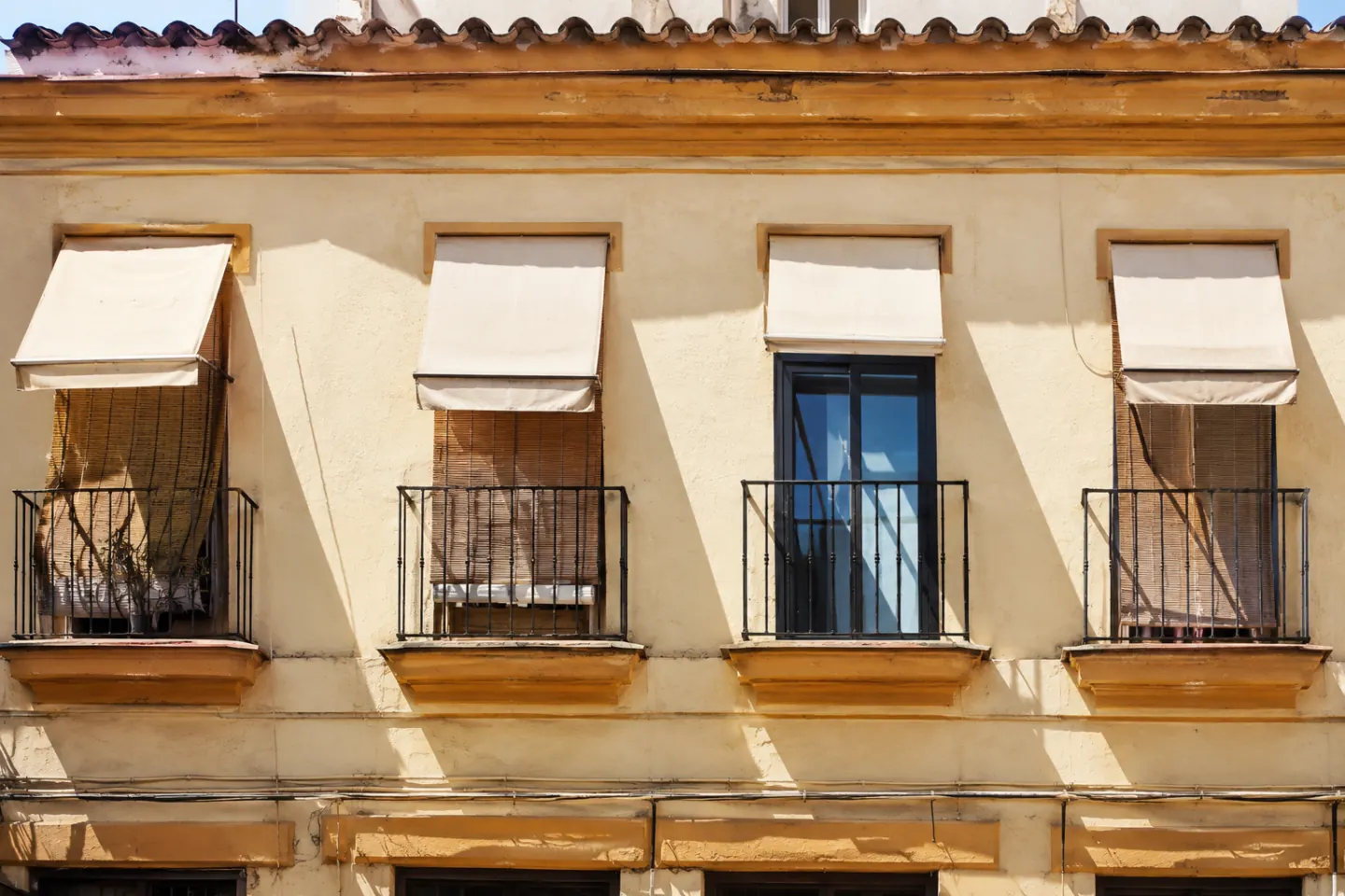 Fachada al sol con toldos bajados y persianas, y una ventana con vidrio nuevo