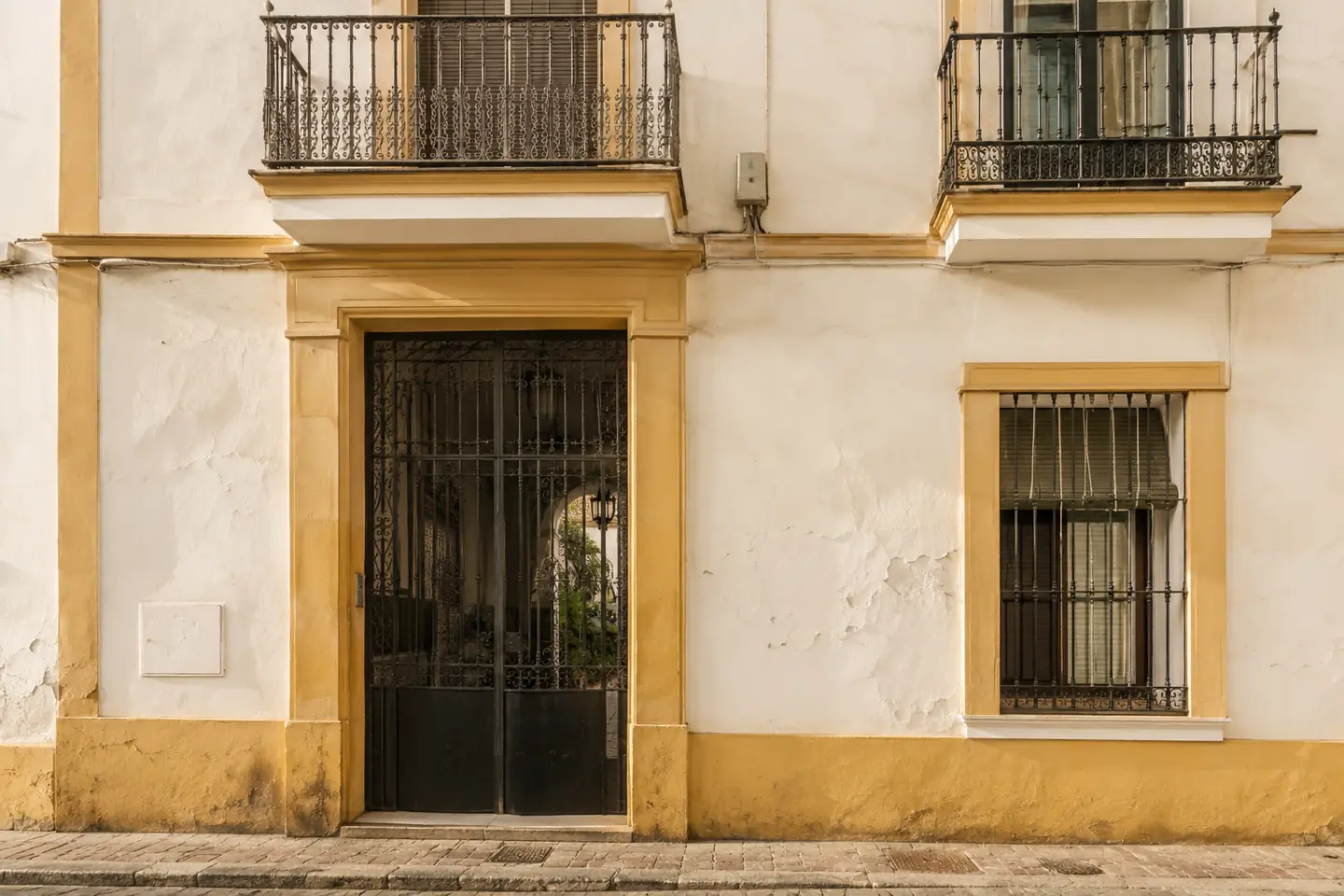 Fachada de un edificio antiguo del centro de Sevilla con placa de número, portal de cancela y balcones de forja