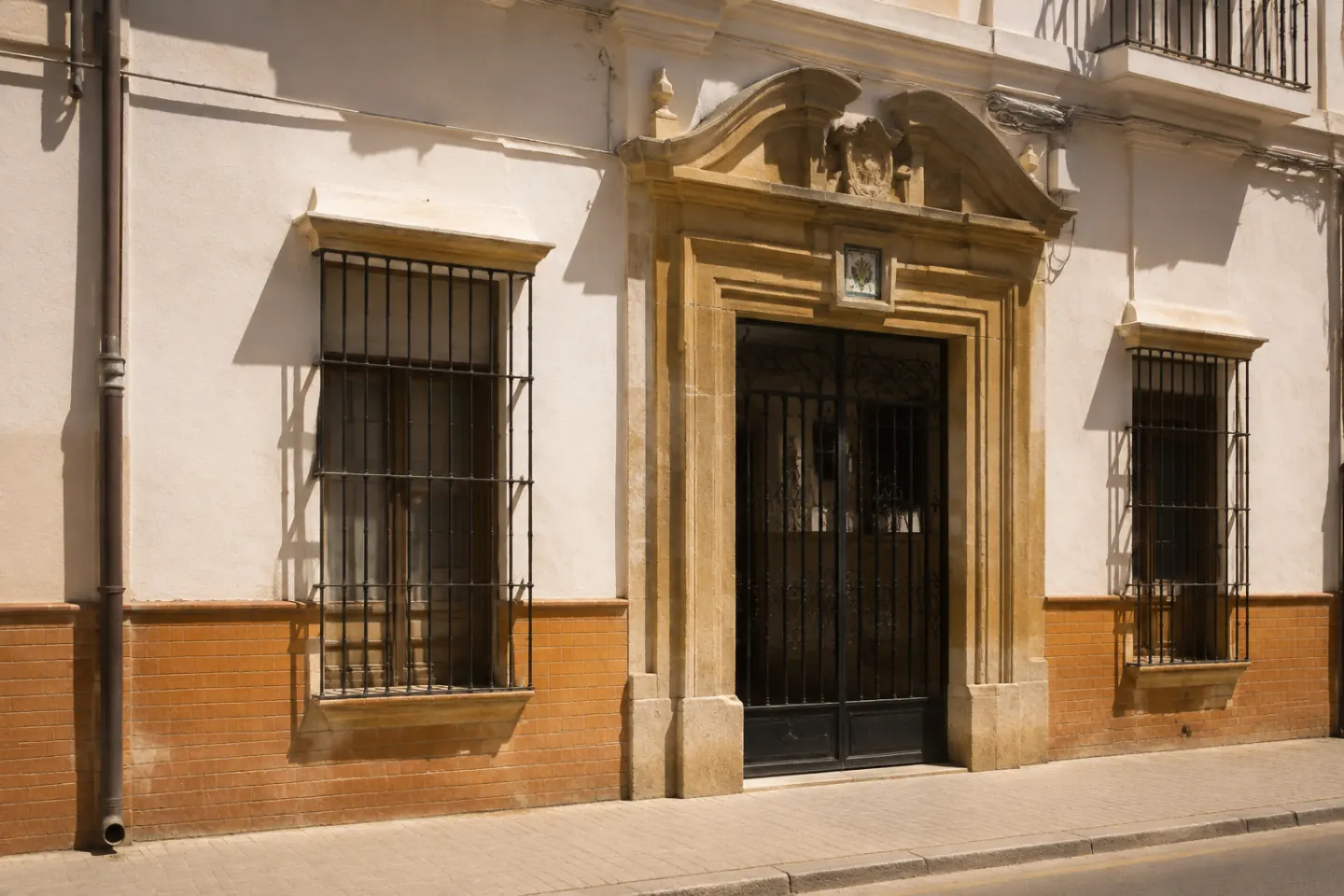 Portada de piedra de un edificio catalogado del casco de Sevilla con cancela de forja y azulejo de rotulación