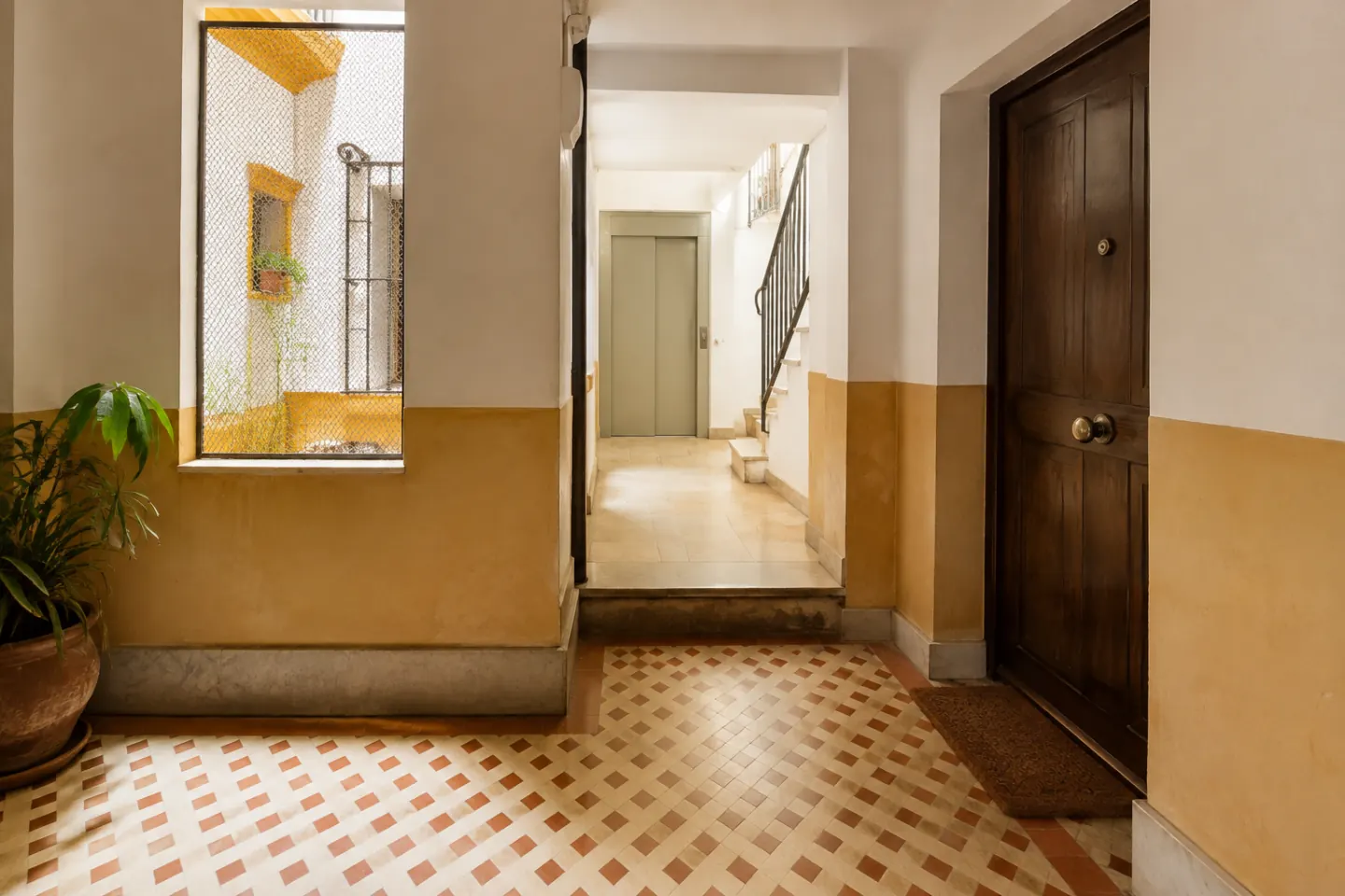 Portal residencial con desnivel visible y ascensor al fondo, logotipos ni dirección reconocible